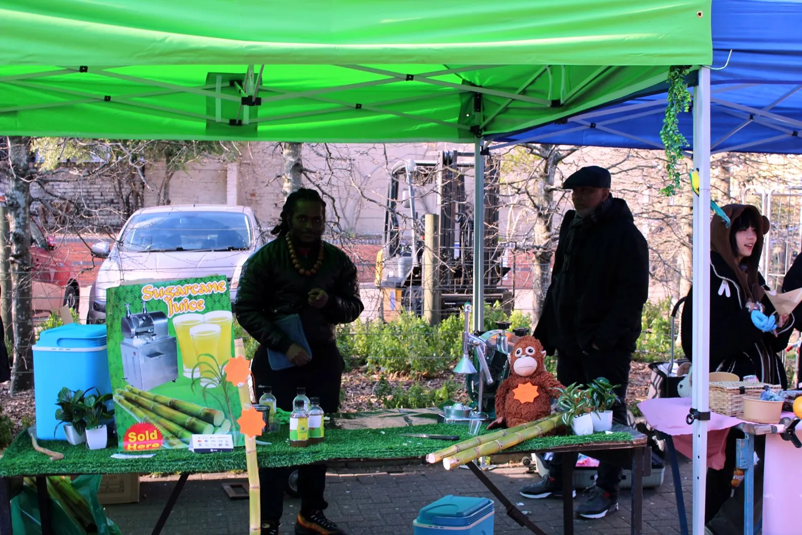 The Sweet Like Cane stall under a green gazebo, with cane stalks and the press on the counter and Jordan and his dad behind it